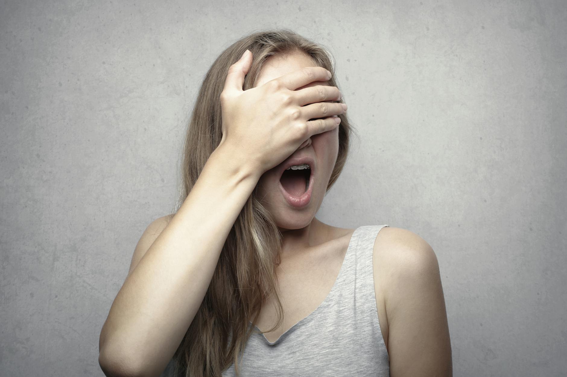 woman in gray tank top covering her face with her hand