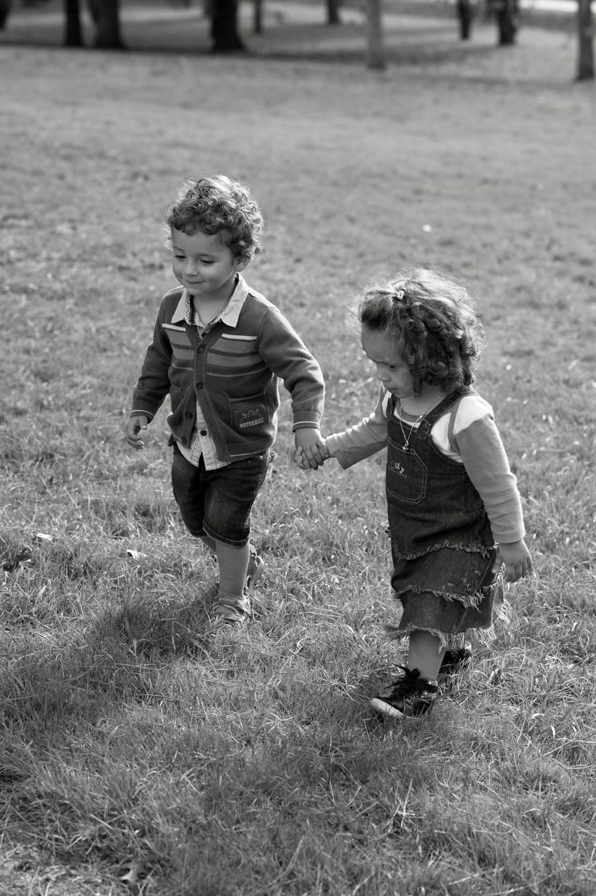 grayscale photo of toddlers walking on grass field